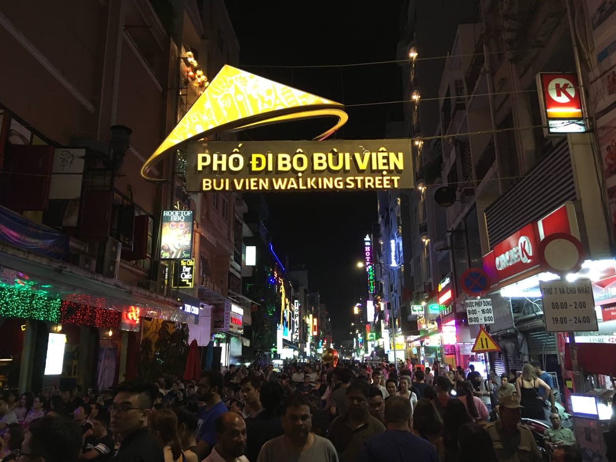 夜晚的裴援步行街，金色的「Phố đi bộ Bùi Viện」招牌橫跨街口，底下滿是人潮與霓虹燈