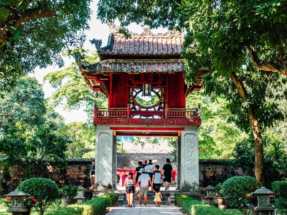 河內文廟的奎文閣，一家人沿著石道走向門樓，兩旁是綠樹與紅色盆花