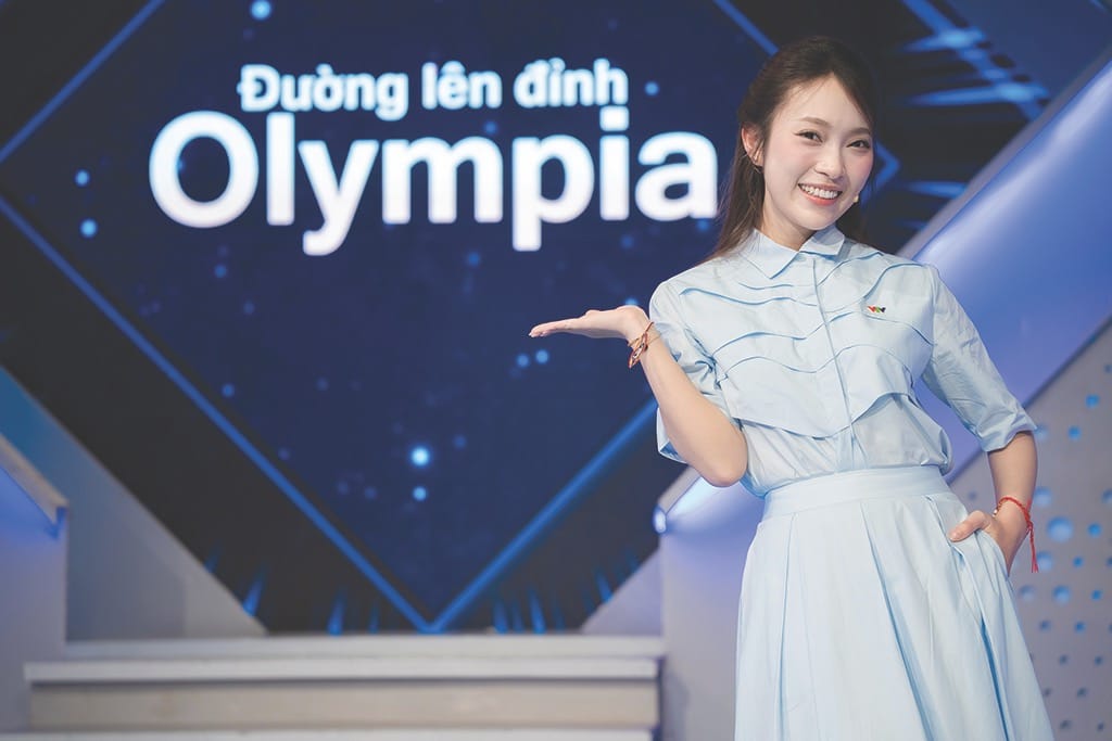 Khánh Vy 站在 Đường lên đỉnh Olympia 節目背板前主持