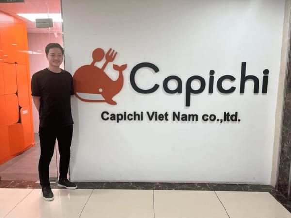 Capichi 創辦人森大樹站在河內辦公室的品牌形象牆旁，牆上有橘色鯨魚 Logo 與 Capichi Viet Nam 字樣