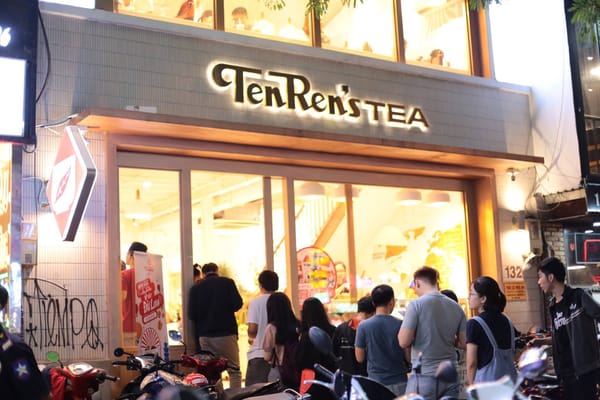 天仁茗茶在越南的門市夜間外觀，TenRen's TEA 招牌亮著燈，門口聚集顧客與停放的機車