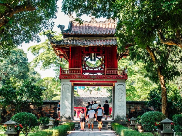 河內文廟的奎文閣，一家人沿著石道走向門樓，兩旁是綠樹與紅色盆花